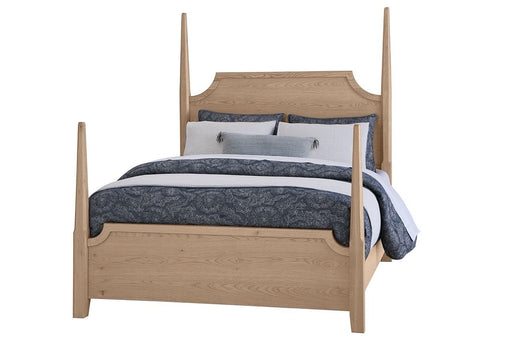 A pencil post bed with a wooden headboard and footboard in a clear oak finish, featuring a mattress and bedding.